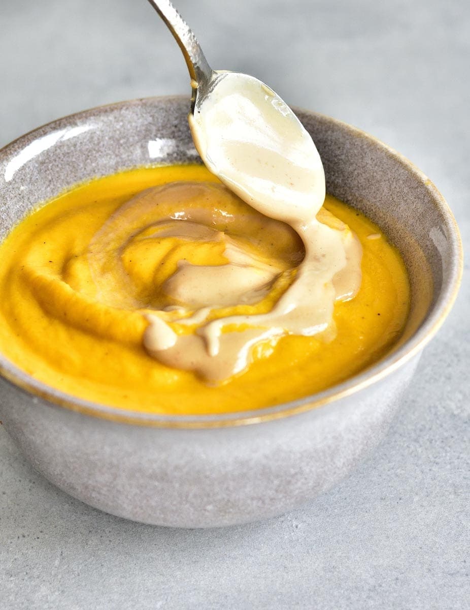peanut butter sauce is being spooned over carrot coconut soup