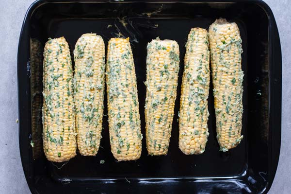 corn on the cob covered in herb and chili butter in a roasting pan