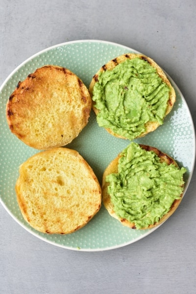 toasted brioche hamburgers buns topped with smashed avocado on a green plate