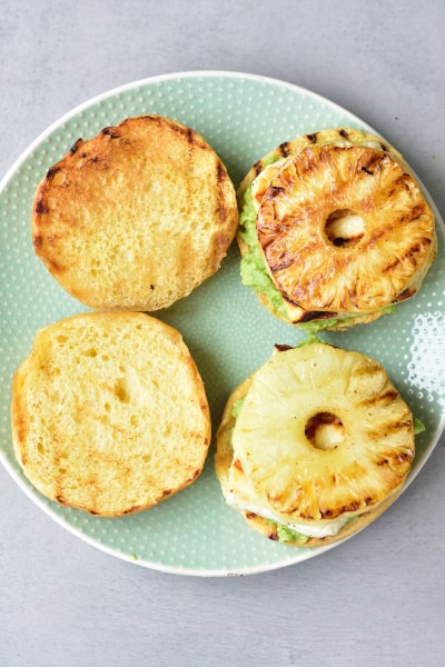 hamburger buns with avocado, grilled halloumi and pineapple on a green plate