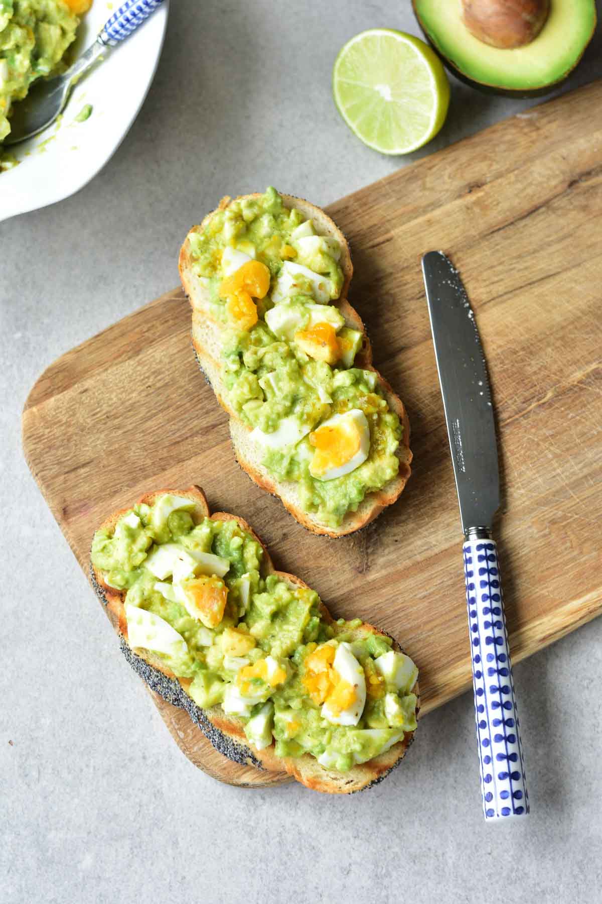 Two slices bread with avocado egg salad on a wooden board.