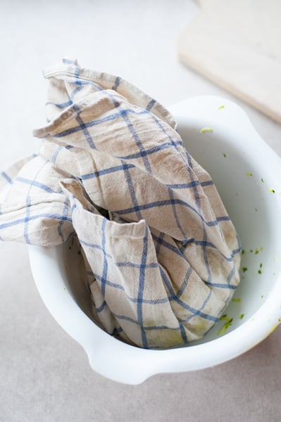 grated zucchini wrapped in a kitchen towel in a white bowl