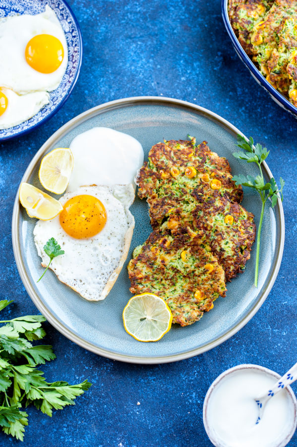 zucchini and corn fritters with fried egg on the side on a blue plate