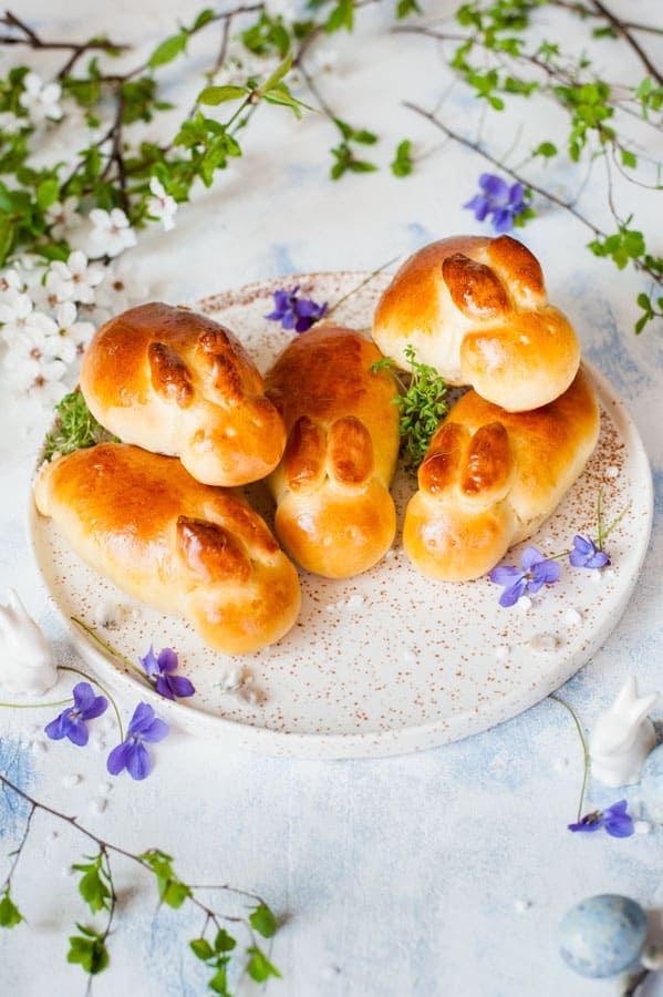 Easter bunny rolls on a white plate with lots of spring flowers in the background