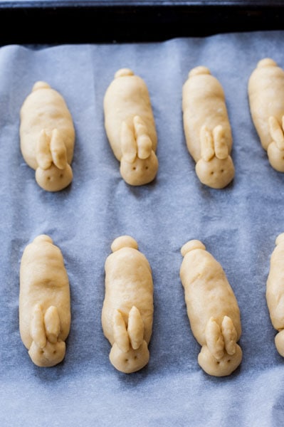 Raw easter bunny rolls on a baking tray linked with baking paper