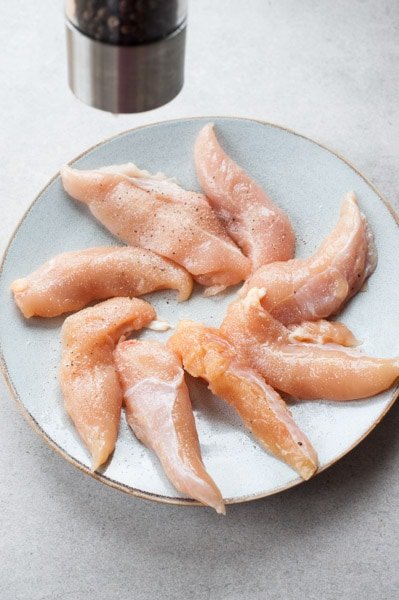 Chicken tenderloins are being seasoned with salt and pepper