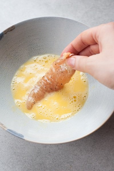Chicken tenderloin is being dipped in beaten egg