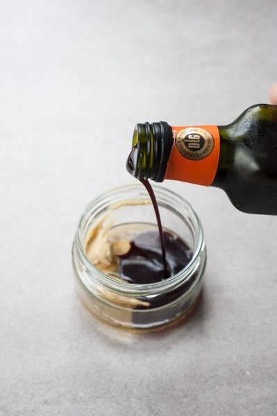 Pumpkin seed oil is being poured into a jar with dressing ingredients