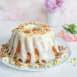 almond bundt cake on a white plate, covered with chocolate glaze and flaked almonds