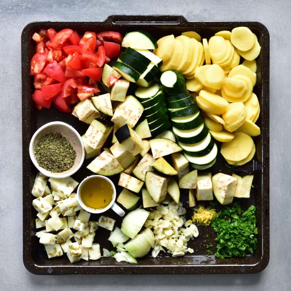 Chopped and sliced vegetables and aromatics needed to prepare briami greek style casserole on a black tray