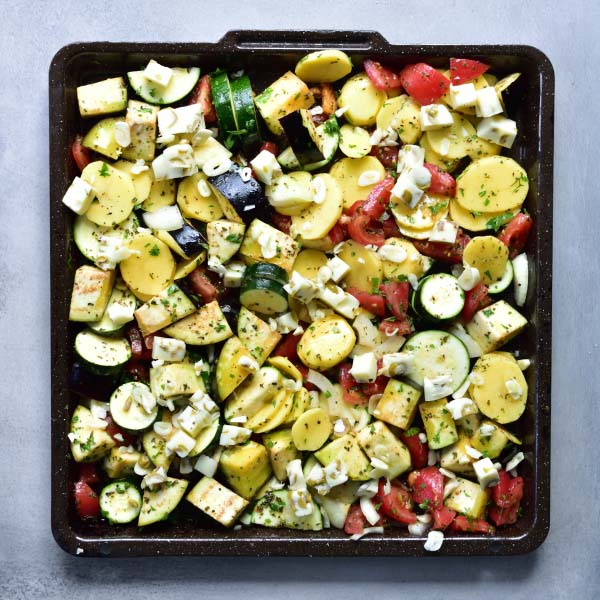 chopped vegetables and cheese mixed on a black baking tray