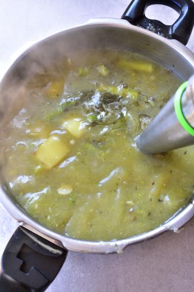 cream of asparagus soup with goat cheese is being pureed with an immersion (stand) blender