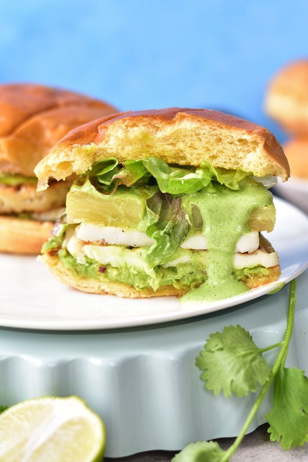 halloumi burgers with pineapple and avocado cut in half and green sauce flowing over the bun