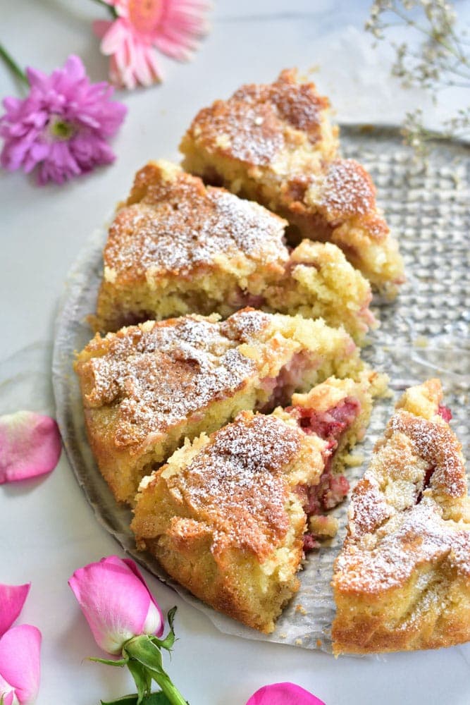 Strawberry coconut cake cut into servings, flowers scattered around