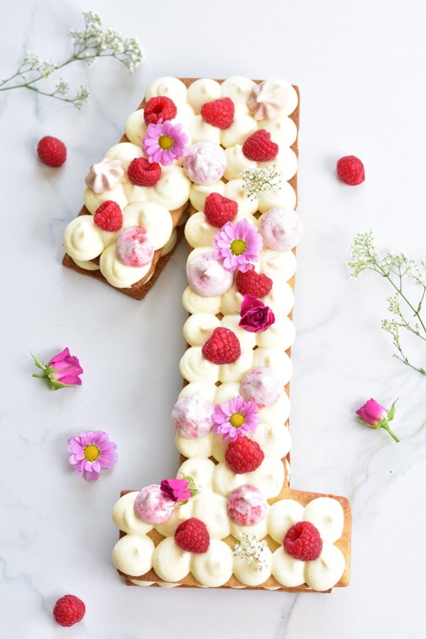 A numer one-shaped number cake decorated with flowers and raspberries.
