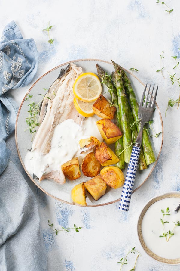 Whole roasted trout with potatoes, asparagus and thyme-garlic dip on a plate