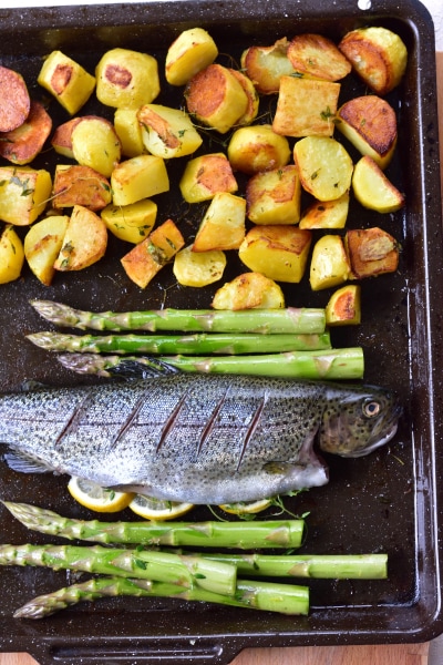 Potatoes, whole trout and asparagus on a baking tray