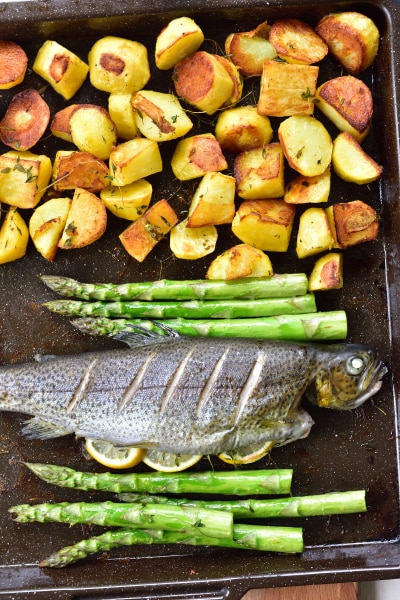 Ready whole roasted trout, potatoes and asparagus on a baking tray