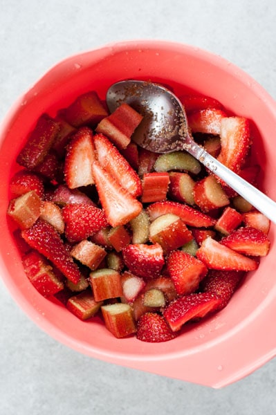 chopped strawberries and rhubarb tossed with sugar in a red bowl