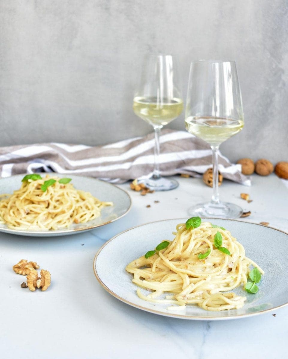 Gorgonzola walnut pasta on two blue plates, white wine in glasses on the side.