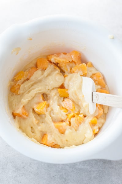 mango muffins batter combined with cubed mango in a white bowl