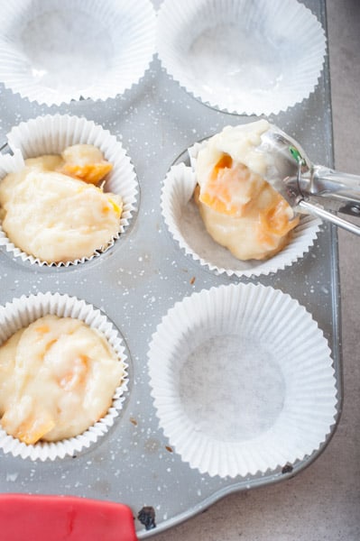 mango muffins batter is being poured into paper muffin cups
