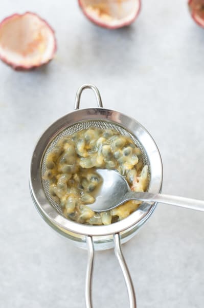 passion fruit seeds are being pressed with a teaspon into a fine mesh strainer