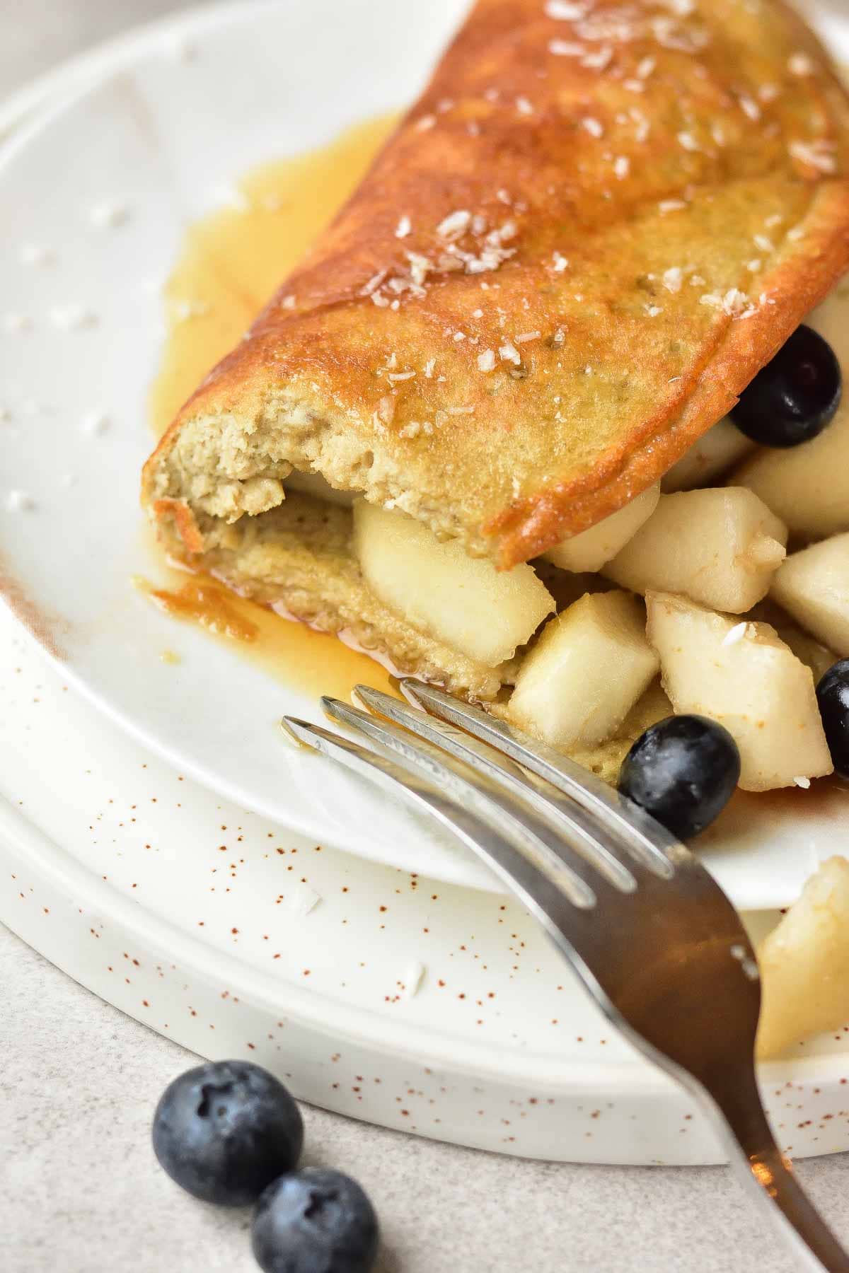 Close up picture of banana oat omelette with pears, blueberries and maple syrup on a white plate.