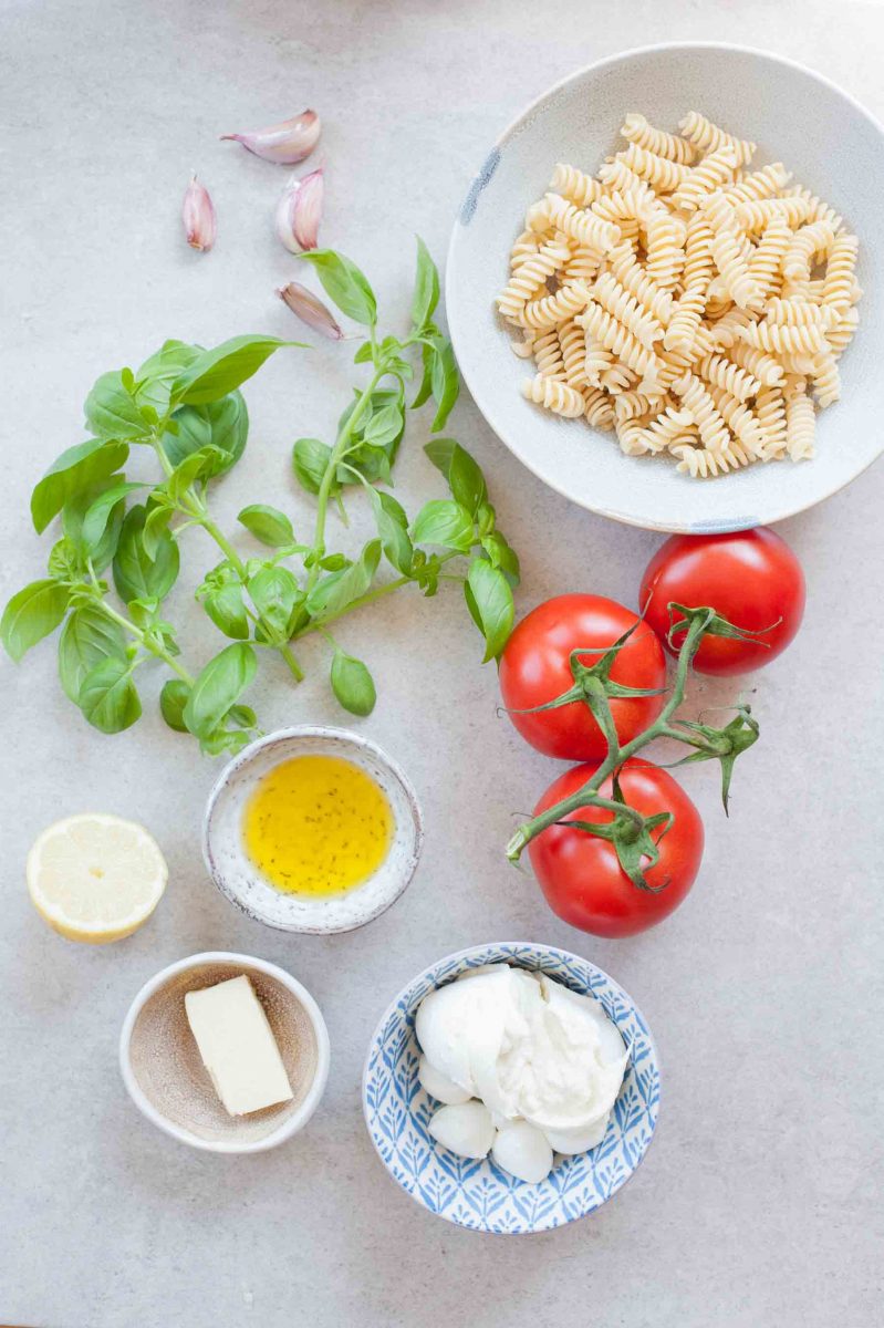 Ingredients needed to make pasta Caprese on a table.