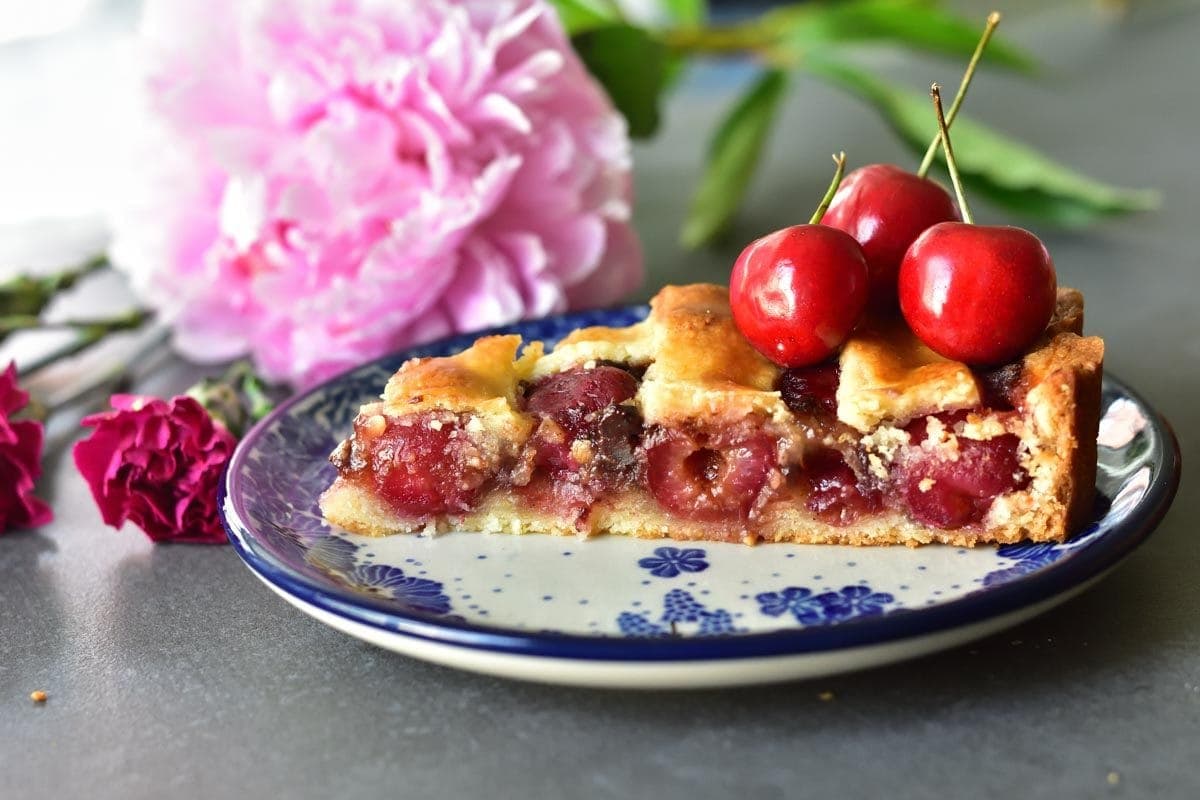 a piece of cherry tart on a white-blue plate, topped with fresh sweet cherries