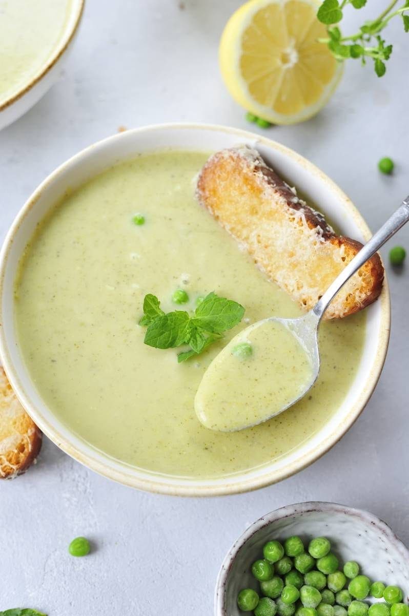 close up photo of creamy zucchini soup with mint and peas in a white bowl