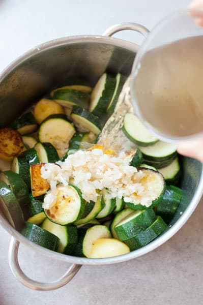 broth is being poured over the browned zucchini and potatoes in a pot