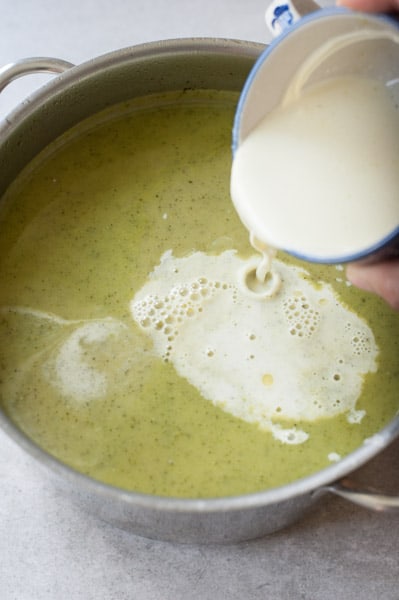 tempered cream is being poured into zucchini soup in a pot