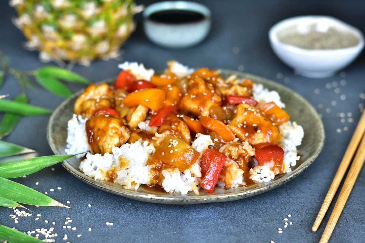 Close up picture of a sweet and sour chicken with pineapple and bell peppers with rice on a plate.