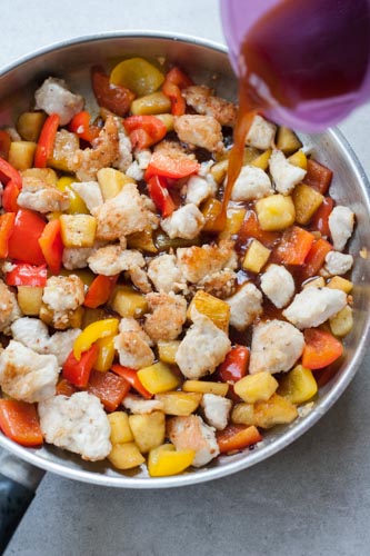 sauce is being added to pan-fried chicken, bell paprika and pineapple on a pan