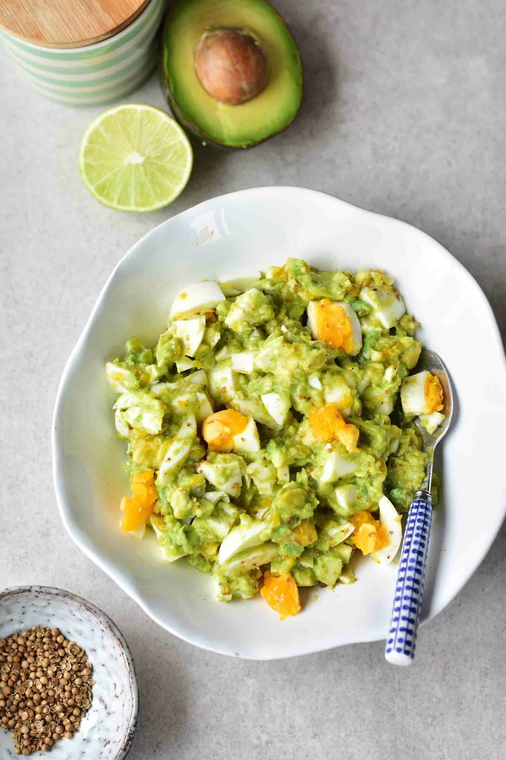 Avocado egg salad in a white bowl. Avocado and lime in the background.