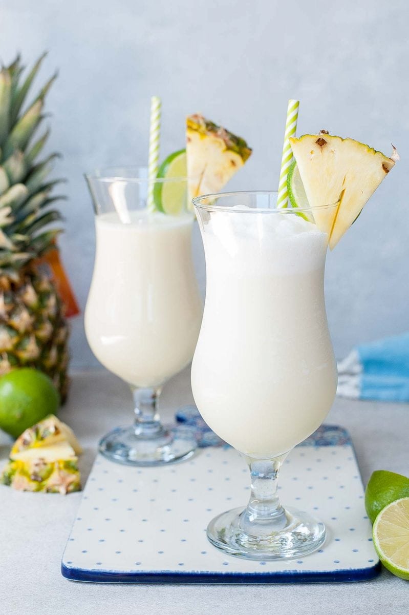 Pina colada in two glasses on a white-blue serving board.