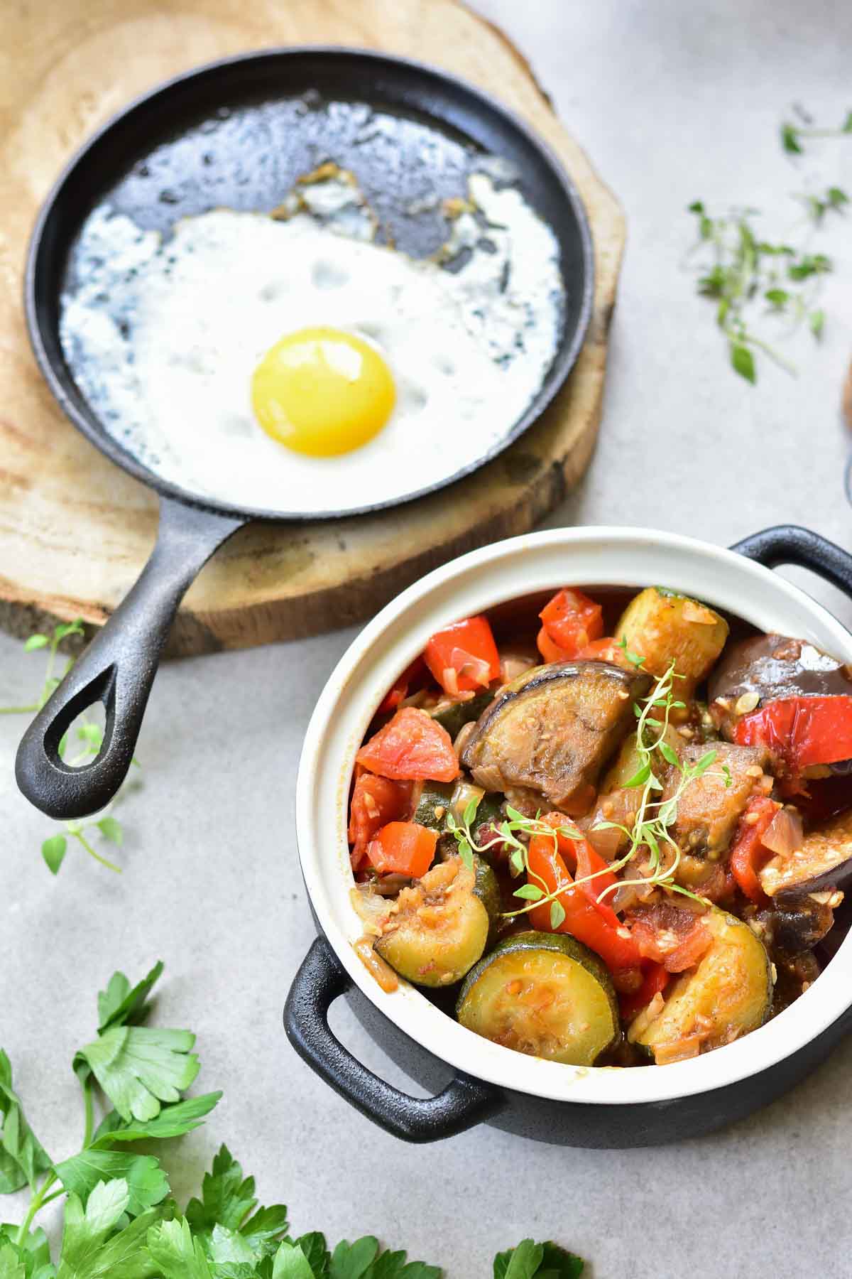 Ratatouille in a pot and a fried egg in a pan on the side.