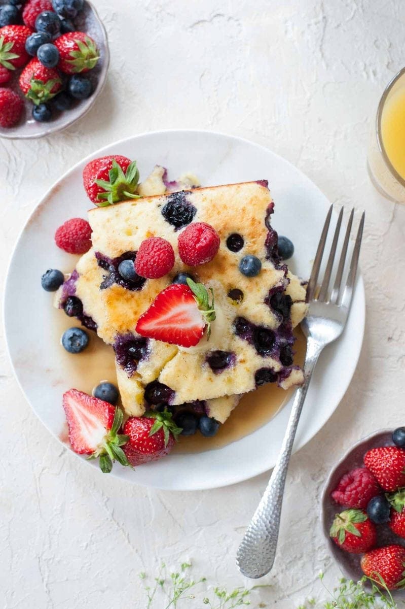 An overhead photo of a stack of sheet pan pancakes and fresh berries on a white plate.