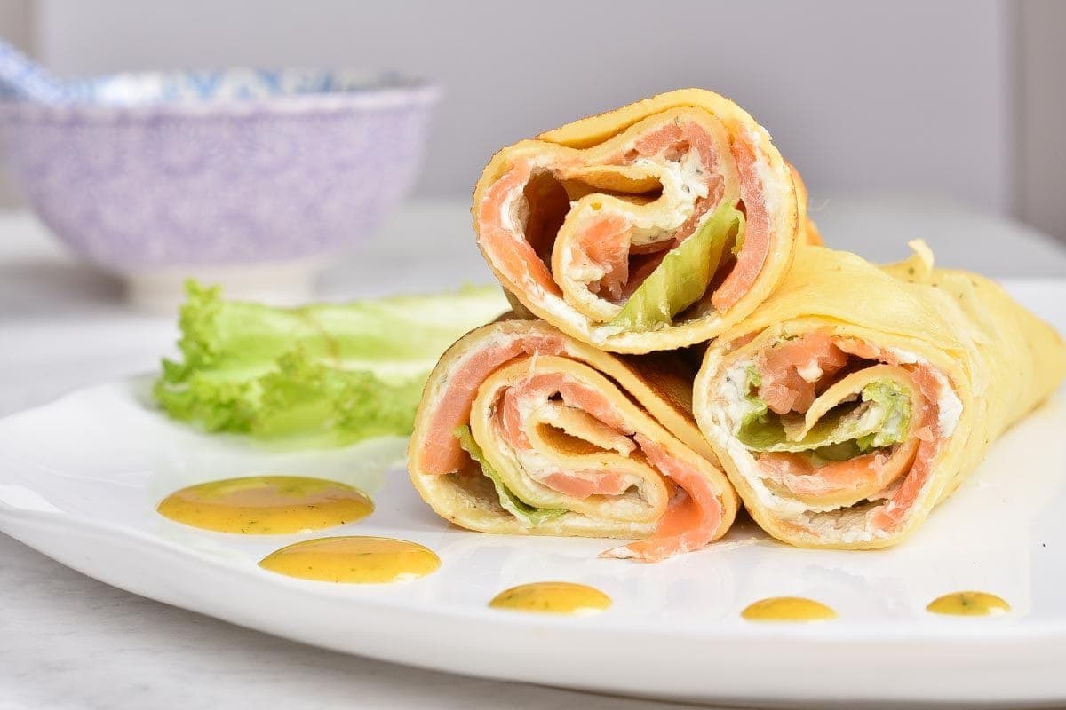 smoked salmon pancakes with honey mustard sauce on a white plate cut in half, close up shot