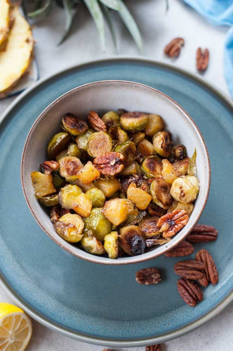 close up picture of roasted brussel sprouts with pineapple and pecans in a bowl