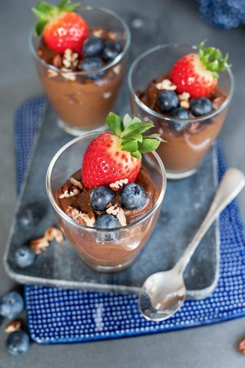 Close up picture of 3 glasses with healthy chocolate pudding topped with fresh berries.