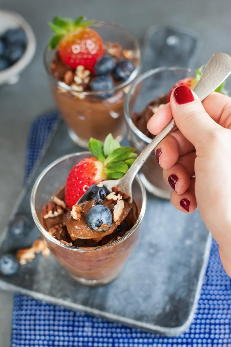 Healthy chocolate pudding is being scooped out of a glass with a teaspoon.