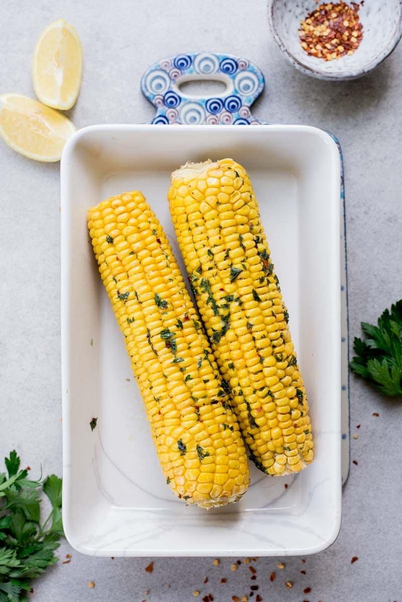 oven-roasted corn on a cob in a white baking dish