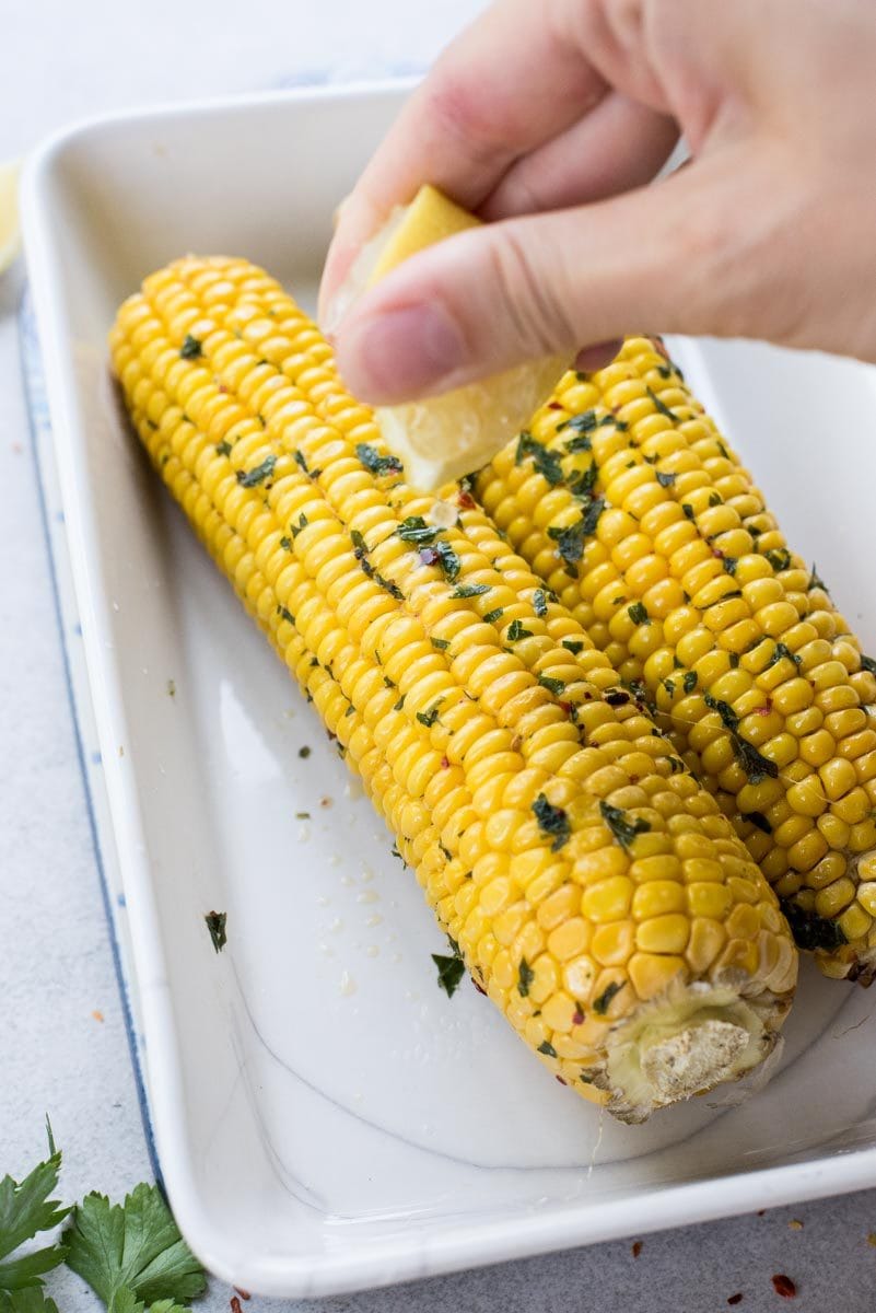 lemon is being juiced over a oven-roasted corn on a cob