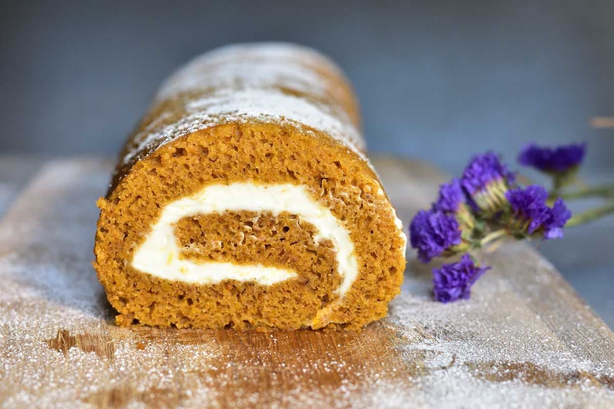 Pumpkin roll with orange cream cheese cut in half, on a wooden board.