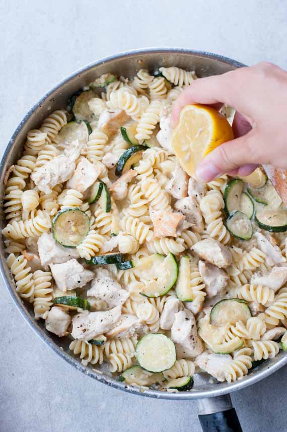 lemon is being juiced over a pan with zucchini chicken pasta