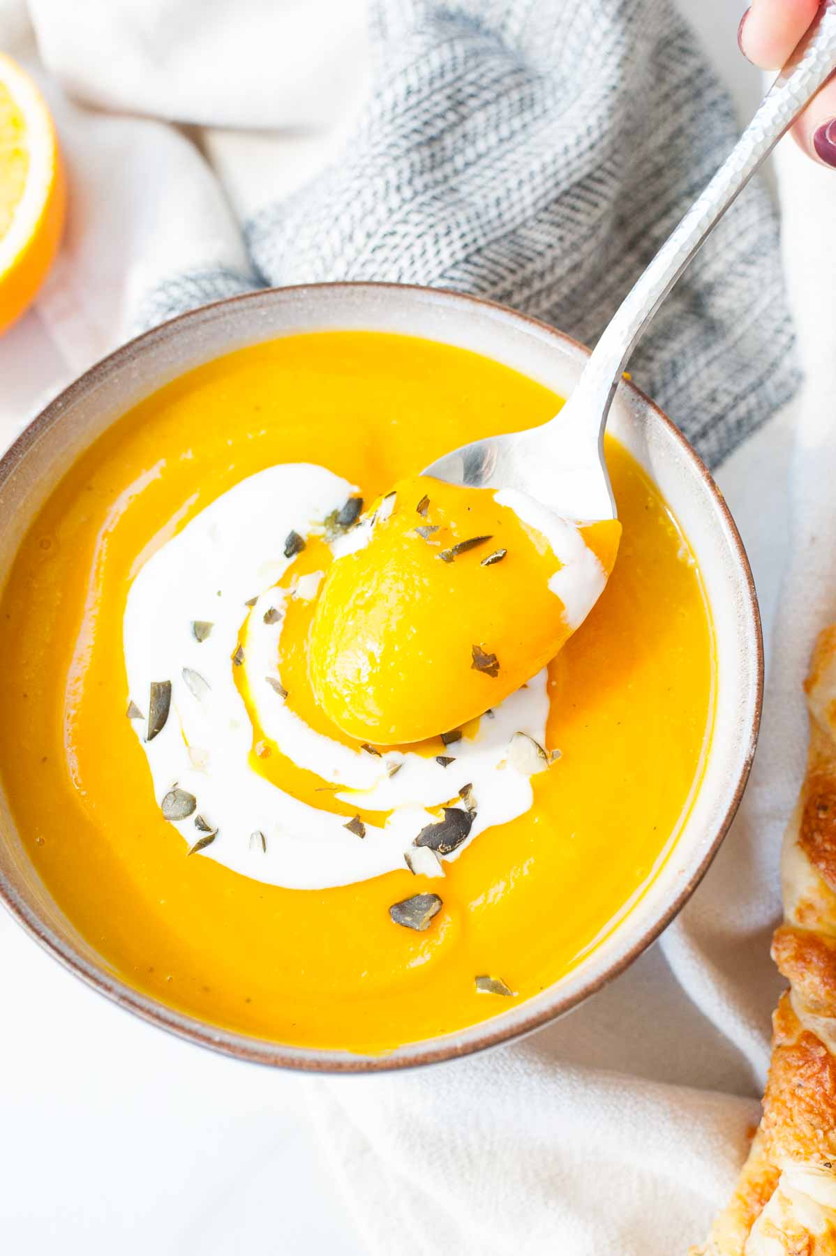 Pumpkin and ginger soup with orange is being scooped with a spoon.