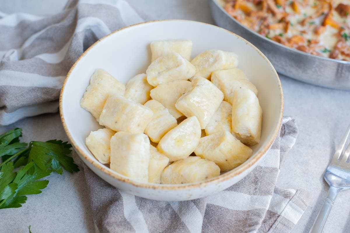 Ricotta gnocchi in a white bowl. Mushroom sauce in a pan in the background.