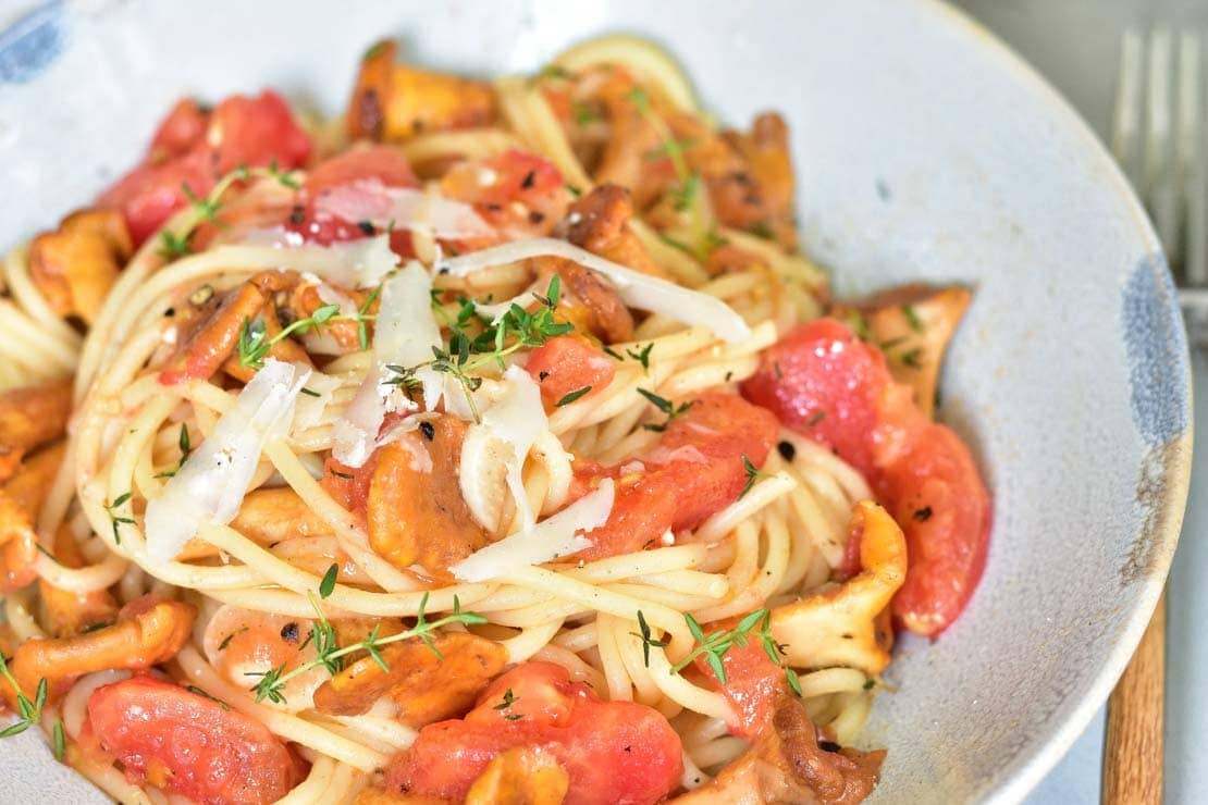 close up photo of pasta with chanterelles and tomatoes in a blue bowl